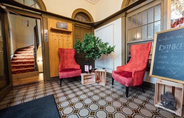 Im Eingangsbereich stehen zwei rote Sessel und eine Tafel, im Hintergrund sieht man eine geschwungene Treppe | © Touristikgemeinschaft Hohenlohe e. V.