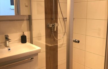Modernes Badezimmer mit weißem Waschbecken, Spiegelschrank und begehbarer Dusche mit Holzoptik und Glasabtrennung | © Brennerei Stilling