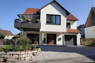 Modernes zweistöckiges Haus mit weißer Fassade, rotem Ziegeldach, Balkon mit Pflanzen und gepflasterter Einfahrt | © Simone Bürckert