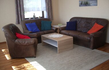 Wohnzimmer mit braunen Ledersofas, bunten Kissen, einem hellen Holztisch und einem grauen Teppich auf Holzboden | © Ferienwohnung Ehrmann