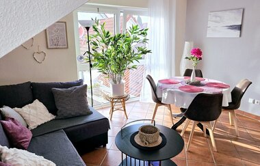 Wohnzimmer mit dunkelgrauem Ecksofa, runden schwarzen Couchtisch, großem grünen Pflanzenkübel vor Fenster und Esstisch mit vier Stühlen und rosa Tischsets | © Familie Fuhrmann