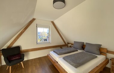 Schlafzimmer mit Doppelbett mit grauer Bettwäsche, Holzboden, einem Fenster und einem schwarzen Sessel mit Kissen | © Ferienwohnung Etzl