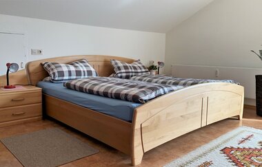 Holzbett mit karierten Bettdecken und Kissen, Nachttisch mit Lampe, Teppich und Pflanze in einem hellen Schlafzimmer