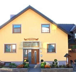 Gelbes Einfamilienhaus mit brauner Haustür, vier Fenstern und einem kleinen Garten mit Blumen. | © Gästehaus Mittnacht