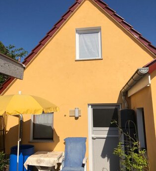 Gelbes Haus mit rotem Dach, weißer Tür, grauer Garage und Terrasse mit blauem Stuhl, gelbem Sonnenschirm und kleinem Tisch | © Gästehaus Sabine