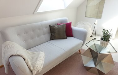 Sitzecke mit weißer Couch, rot und grauem Kissen und eine weiße Decke. Davor steht ein kleiner Tisch mit Topfpflanze. | © Neckar-Zaber-Tourismus e.V.