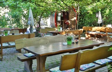 Sonniger Biergarten mit Holztischen und Bänken, umgeben von grünen Bäumen und Pflanzen | © Landgasthof Taubertal