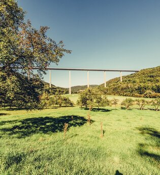 Hier ist die Kochertalbrücke von weiten zu sehen, im Vordergrund kann man sehr viele Bäume und die Natur sehen. | © Arbeitsgemeinschaft Kocher-Jagst-Radweg