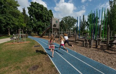 Drei Kinder rennen auf einer blauen Laufbahn um die Wette