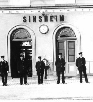 Antikes Schwarz-Weiß-Foto mit Bahnmitarbeitern in Uniformen vor dem Bahnhofsgebäude Sinsheim | © Unbekannt