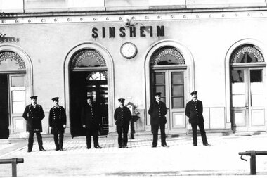 Antikes Schwarz-Weiß-Foto mit Bahnmitarbeitern in Uniformen vor dem Bahnhofsgebäude Sinsheim | © Unbekannt