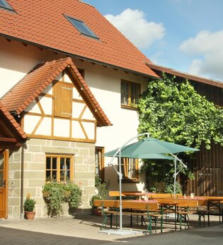 Die Weinstube hat außen eine Sommerterrasse mit Biertischen und Sonnenschirmen | © Touristikgemeinschaft Hohenlohe e. V. | Baldeles Weinstube