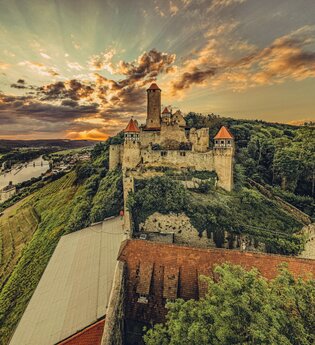 Blick auf eine Burg die auf einem Berg steht. Auf der linken Seite fließt ein Fluss auf der rechten Seite ist ein Wald. Burg Hornberg im Odenwald. | © Touristikgemeinachaft Odenwald e.V.