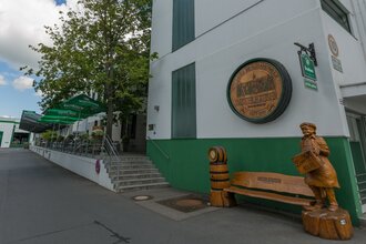 Blick auf den Eingangsbereich der Distelhäuser Brauereigaststätte. Hier steht eine große hölzerne Bank mit einer geschnitzten Figur, die einen Bierkaste trägt. An der Wand hängt ein geschnitzer Fassboden. Im Hintergrund ist die Terasse zu sehen. | © Tourismusverband "Liebliches Taubertal"