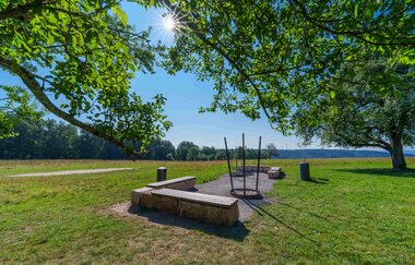 Sonniger Picknickplatz mit Bänken und Feuerstelle auf einer Wiese, umgeben von Bäumen. | © Michael Kuehneisen