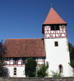 Die Kirche hat einen hohen Turm und rotes Fachwerk | © Touristikgemeinschaft Hohenlohe e. V. | Marion Schlund