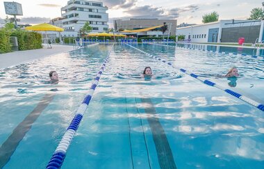 Drei Kinder schwimmen in einem Außenpool mit abgetrennten Bahnen