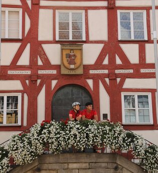 Zwei Personen stehen auf dem Treppenaufgang zum historischen Rathaus mit rotem Fachwerk | © Touristikgemeinschaft Hohenlohe e. V. | Andi Schmid