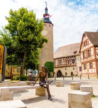 Blick auf den Schlossplatz in Tauberbischofsheim. Im Hintergrund ist der Türmersturm mit dem Kurmainzischen Schloss zu sehen. Im Vordergrund ein Brunnen mit Figuren aus Kupfer. | © Tourismusverband "Liebliches Taubertal" e.V.
