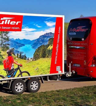Ein roter Bus zieht einen Fahrradanhänger.