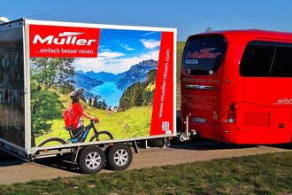 Ein roter Bus zieht einen Fahrradanhänger.