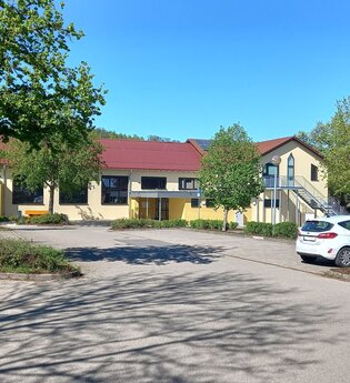 Parkplatz an der gelb gestrichenen Gemeindehalle in Ottendorf mit geparkten Autos und Bäumen im Frühling | © Petra Natzkowski