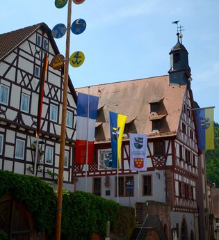 Blick auf das im Fachwerkstil errichtete Rathaus in Freudenberg. Im Vordergrund sind viele Fahnen zu sehen. | © Liebliches Taubertal