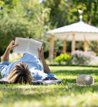 Eine Frag liegt mit auf der Wiese im Schlosspark und liest ein Buch.