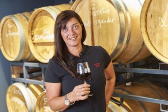 Eine Frau steht mit einem Rotwein vor Weinfässern | © Touristikgemeinschaft Hohenlohe e. V. | Weingut Schneckenhof