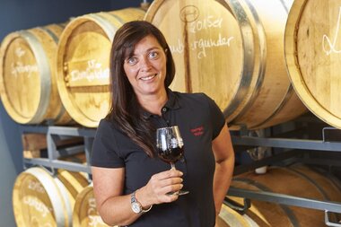Eine Frau steht mit einem Rotwein vor Weinfässern | © Touristikgemeinschaft Hohenlohe e. V. | Weingut Schneckenhof