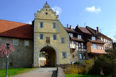 Das Tor ist gelb und hat einen Giebel. Daneben befinden sich Fachwerkhäuser auf der Stadtmauer | © Touristikgemeinschaft Hohenlohe e. V. | Stadt Forchtenberg