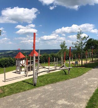 Hölzerne Klettergeräte mit rotem Dach auf sandigem Boden und Rasen