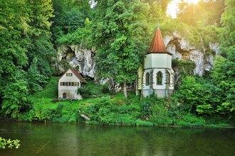 Die Wallfahrtskapelle steht am Fluss Jagst mit einer aufragenden Tuffsteinfelsenwand dahinter