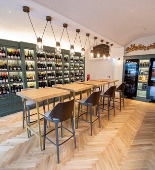 In der Vinothek gibt es Tische und Stühle, an der Wand stehen große Flaschenregale | © Touristikgemeinschaft Hohenlohe e. V.  | Hotel Anne-Sophie