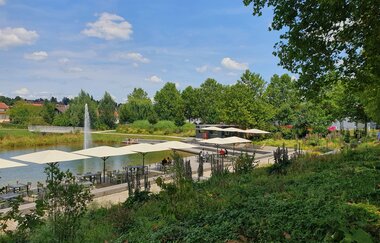 Blick auf den Uferbereich am See im Weiherpark mit Außenbestuhlung einer Gastronomie direkt am See.