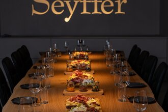 Tagungsraum mit goldenem Schriftzug an Wand "Seyffer", lange Holztafel, eingedeckt mit Essen in der Mitte | © Christian Seyffer