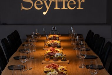 Tagungsraum mit goldenem Schriftzug an Wand "Seyffer", lange Holztafel, eingedeckt mit Essen in der Mitte | © Christian Seyffer