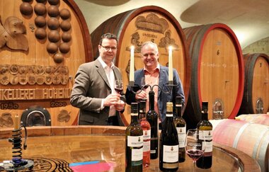 Zwei Männer stehen im Weinkellerer, vorne stehen Weinflaschen und Kerzen brennen | © Touristikgemeinschaft Hohenlohe e. V.