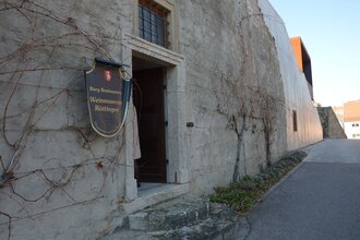 Blick auf den äußeren Eingangsbereich des Weinmuseums in Röttingen. An der Wand hängt ein großes Ritter-Schutzschild mit der Aufschrift "Burg Brattenstein, Weinmuseum Röttingen" . | © Stadt Röttingen