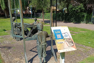 Schild der Weitersehen-Station in Hockenheim vor einer Statue in dem 3 Personen beim Tabakdrehen dargestellt sind
