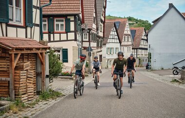 Eine Gruppe von Gravelbikern fährt durch ein idyllisches Dorf mit traditionellen Fachwerkhäusern. | © TMBW
