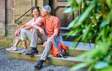 Eine Frau und ein Mann sitzen auf einer Treppe. | © Touristikgemeinschaft Hohenlohe e. V. | Florian Trykowski